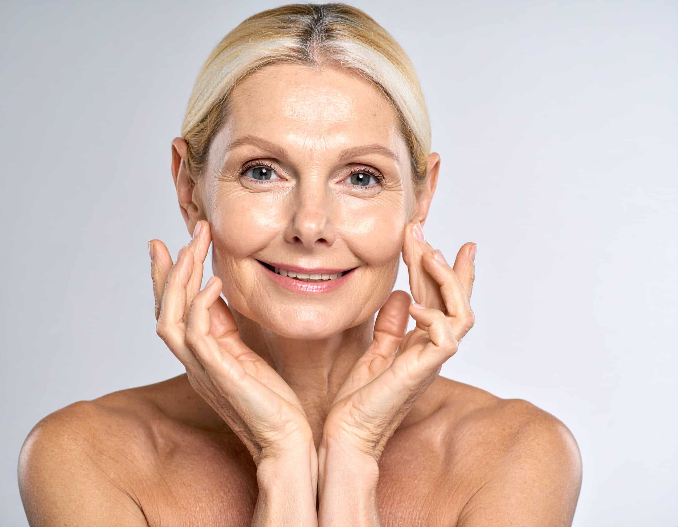 Eine lächelnde Frau mittleren Alters berührt sanft ihre strahlende Haut – Natürliche Unterstützung der Kollagenbildung durch Vitamin C.